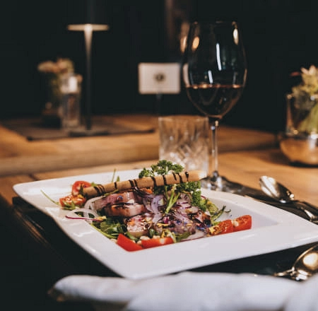 Ein Teller mit Salat und Fisch, Rotwein im Hintergrund.