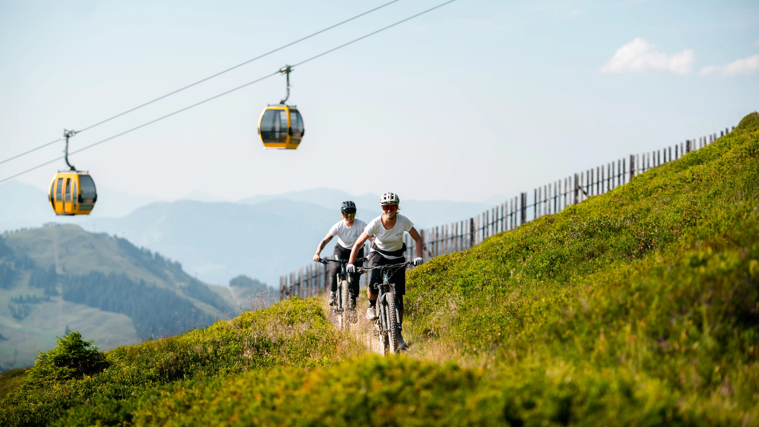 Radfahrer auf einer Bergwiese mit Seilbahn im Hintergrund
