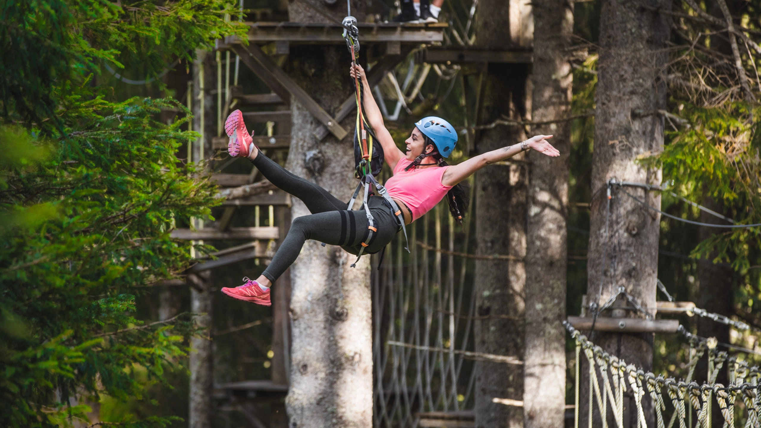 Person schwingt im Hochseilpark zwischen Baumkronen