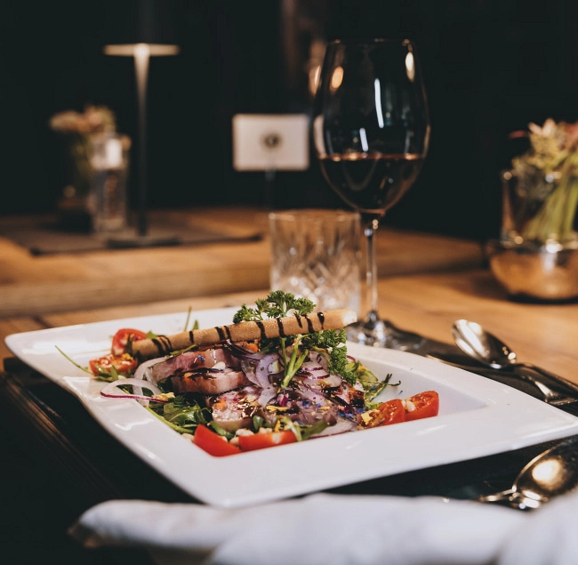 Gourmetgericht auf Teller mit rotem Gemüse und Glas Wein