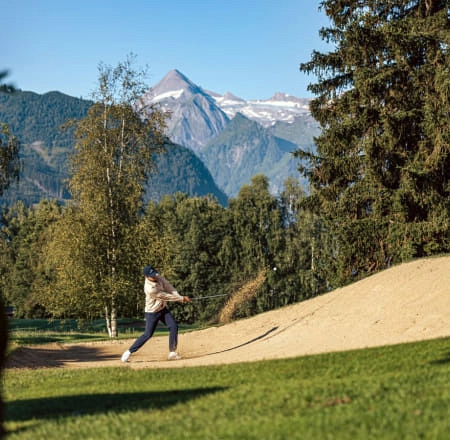 Person spielt Golf in Zell am See, mit Bergen im Hintergrund