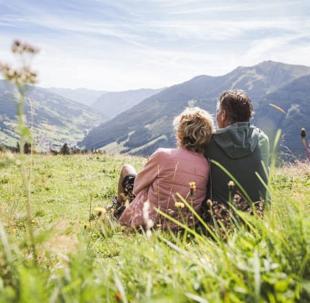 Paar sitzt auf einer Wiese in Saalbach Hinterglemm
