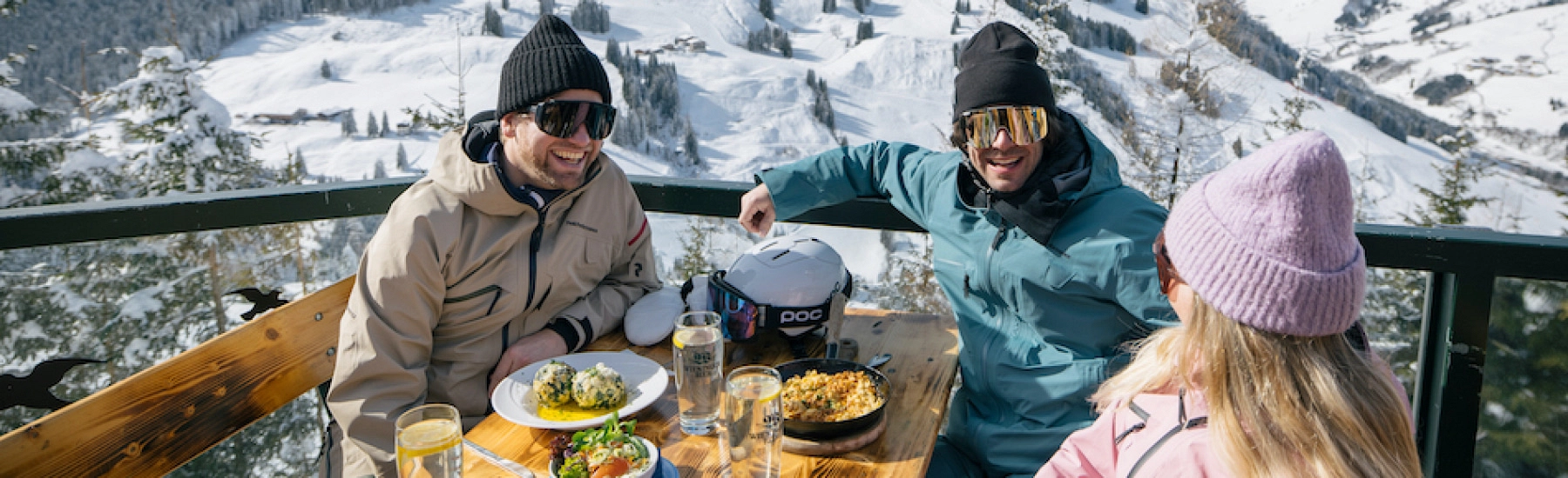 Drei Personen genießen Essen vor schneebedeckter Landschaft.