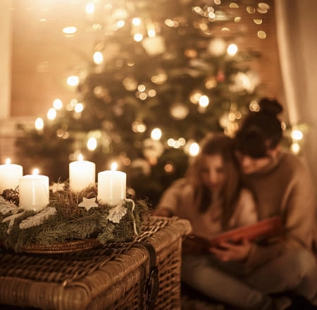 Gemütliche Szene mit Kerzen, Baum und zwei lesenden Personen.
