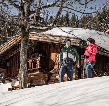 Zwei Personen beim Schneeschuhwandern vor einer Hütte